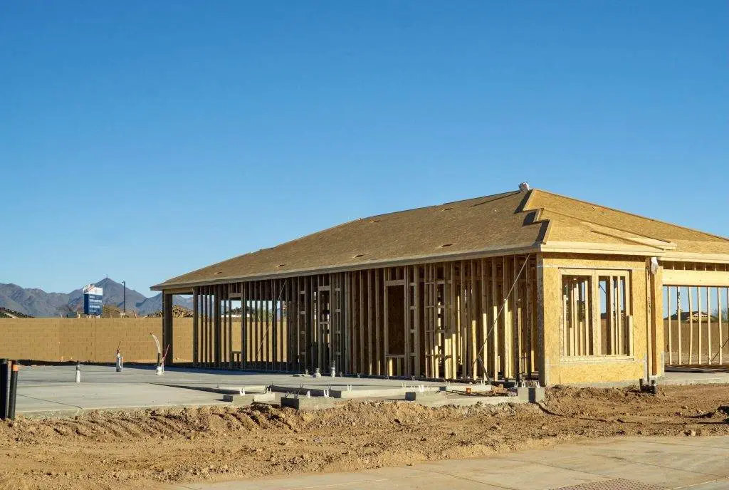 A framed house under construction and a concrete slab foundation with plumbing ready for framing